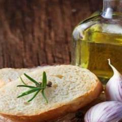 Bottiglia di vetro con olio d'oliva accanto a fette di pane casereccio con rosmarino e spicchi d'aglio freschi
